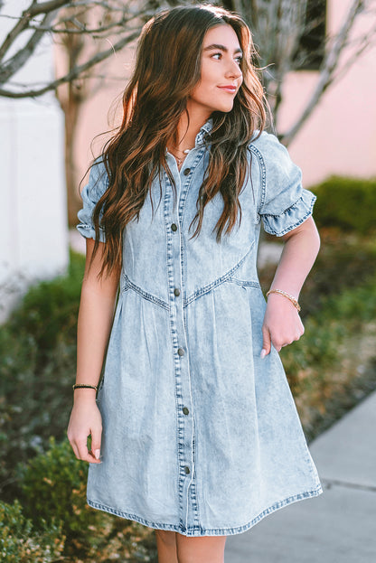 Model relaxing on a park bench in a blue mineral washed denim dress with ruffled short sleeves and pockets.