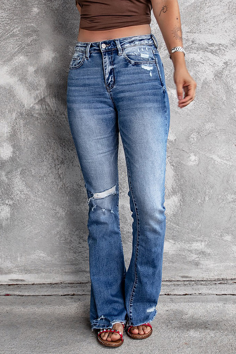 Model wearing dark blue ripped raw hem high waist flare jeans (front view).