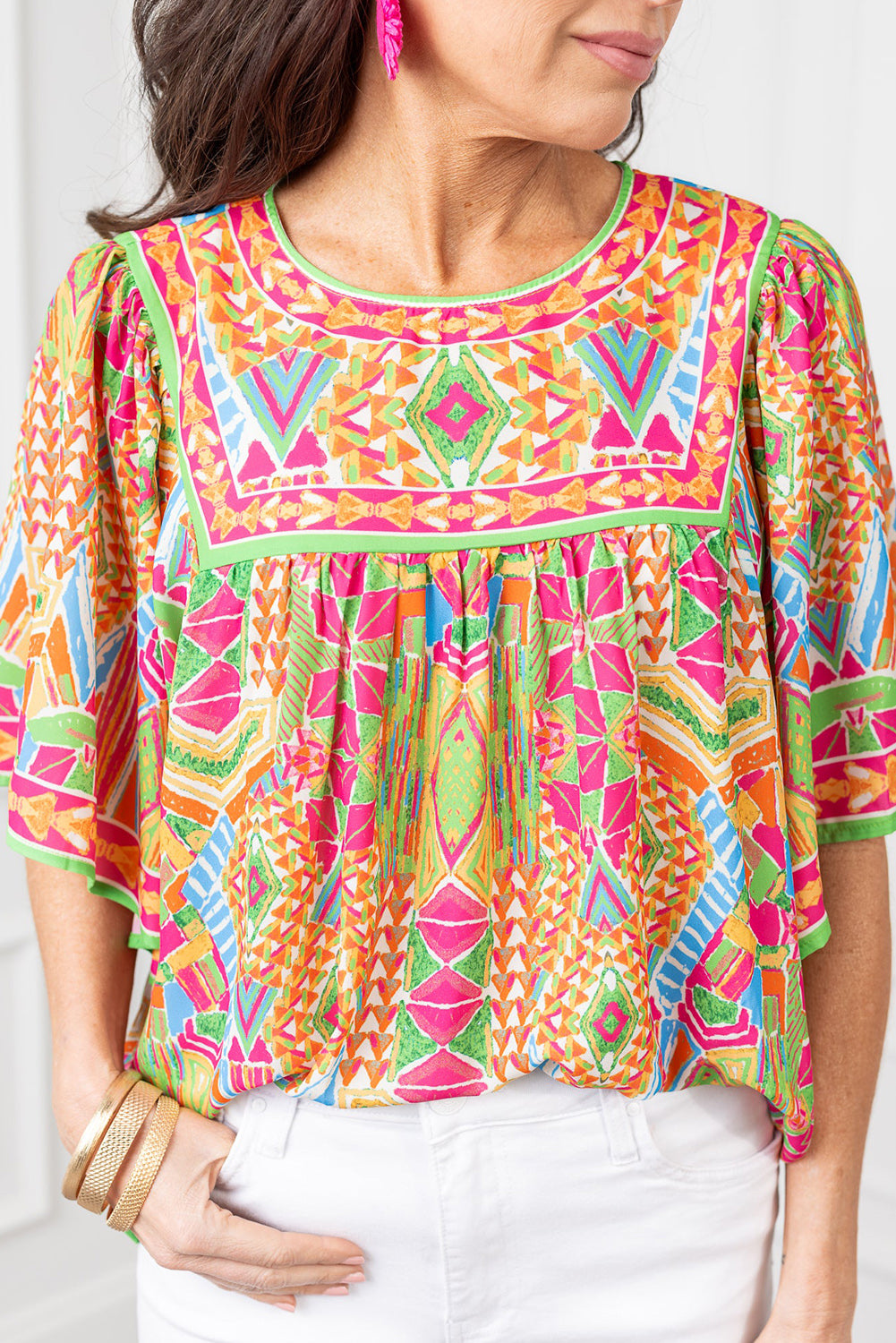 Close-up of the neckline and shoulder with bell sleeves on the orange geometric print blouse.