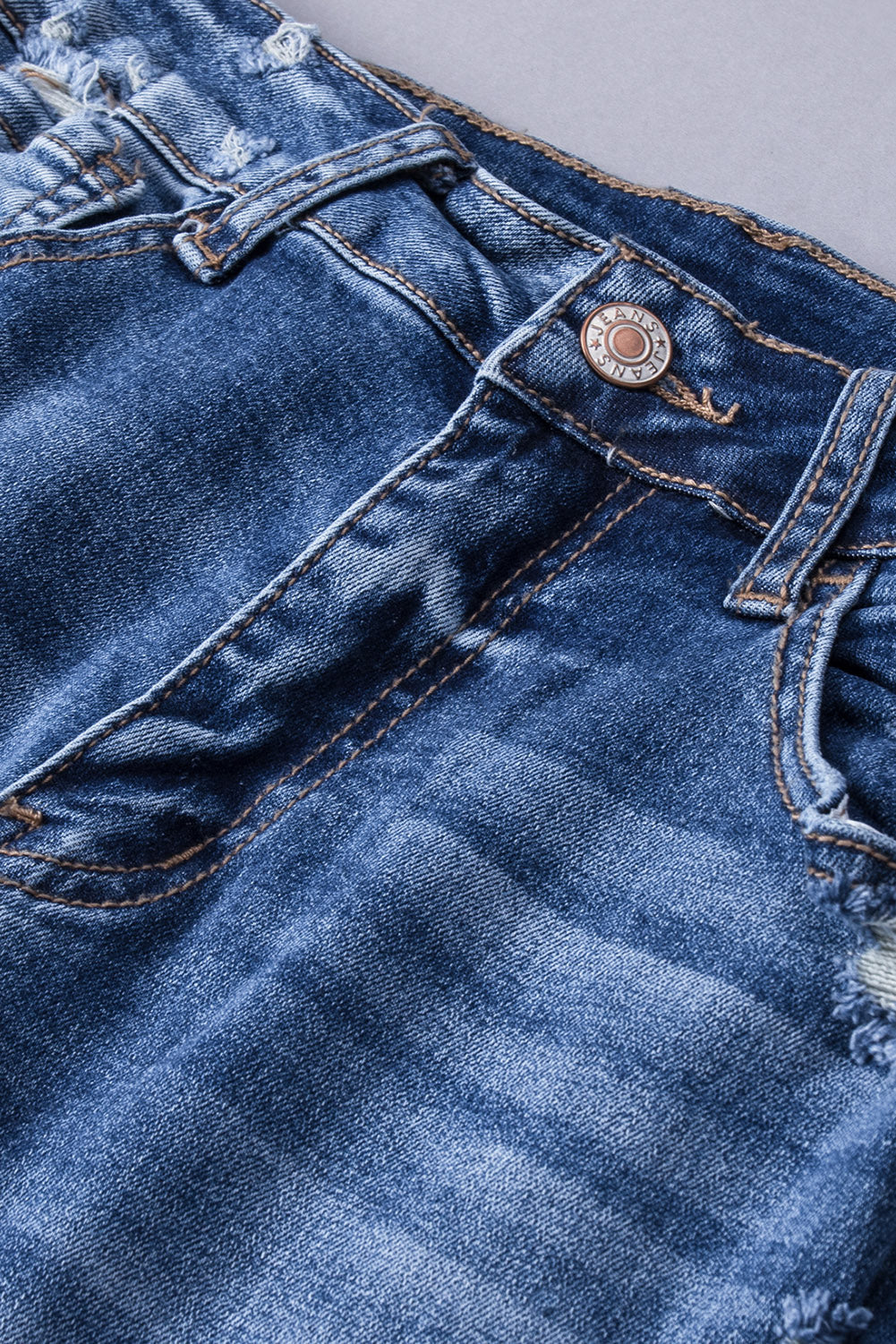 Close-up of the ripped details and raw hem on the dark blue flare jeans.