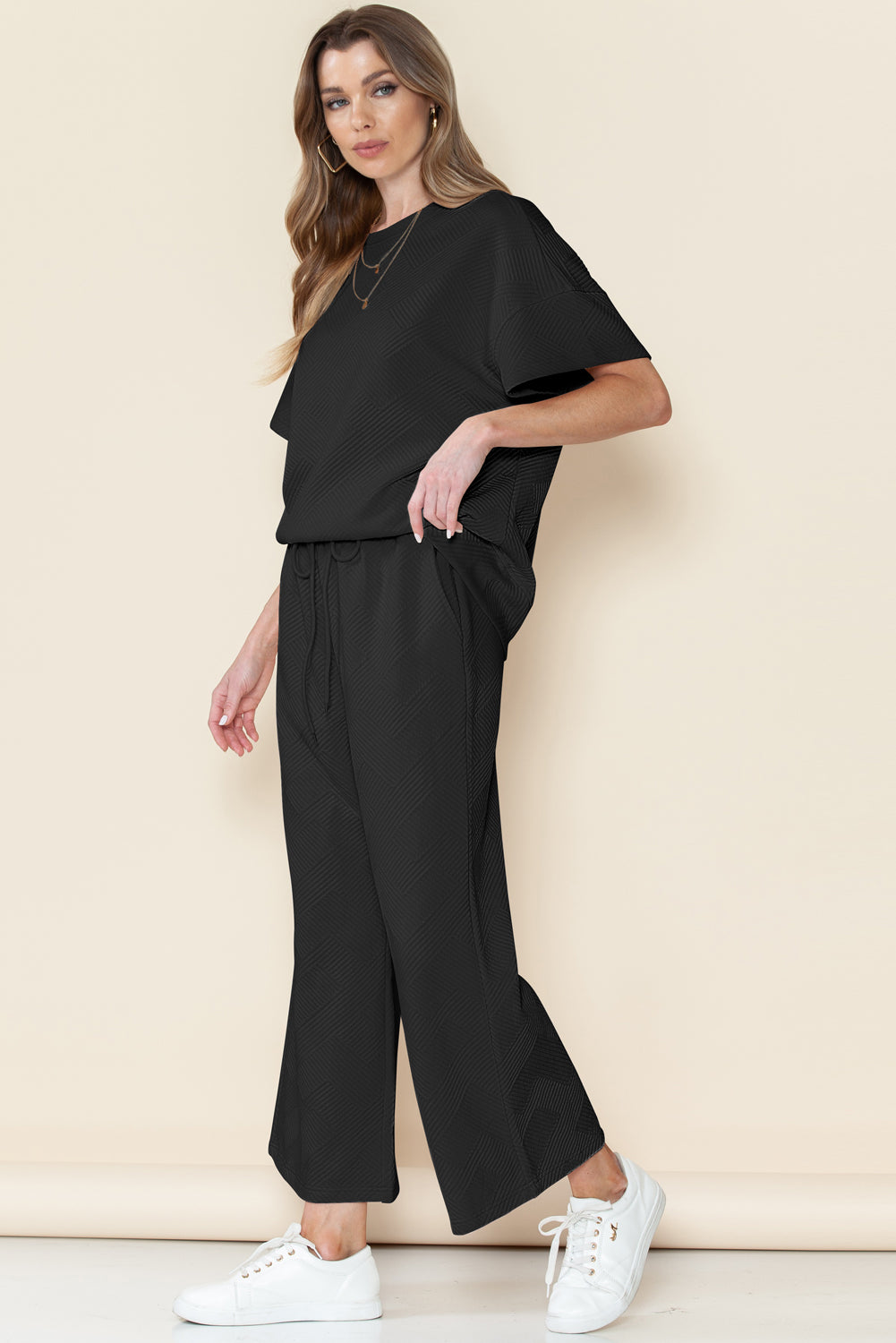 Model walking confidently in black textured T-shirt and drawstring pants set.