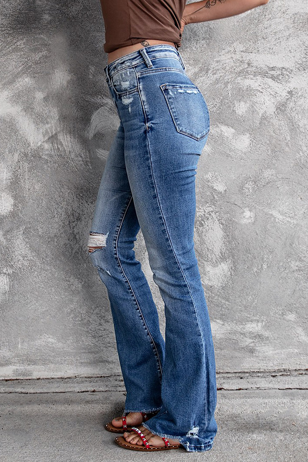 Model walking confidently in dark blue ripped raw hem high waist flare jeans.