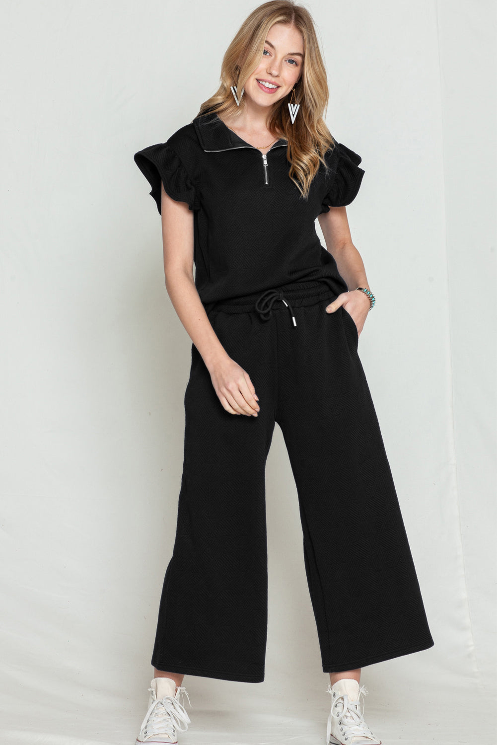 Model walking confidently in black textured ruffle cap sleeve top and wide-leg pants set.