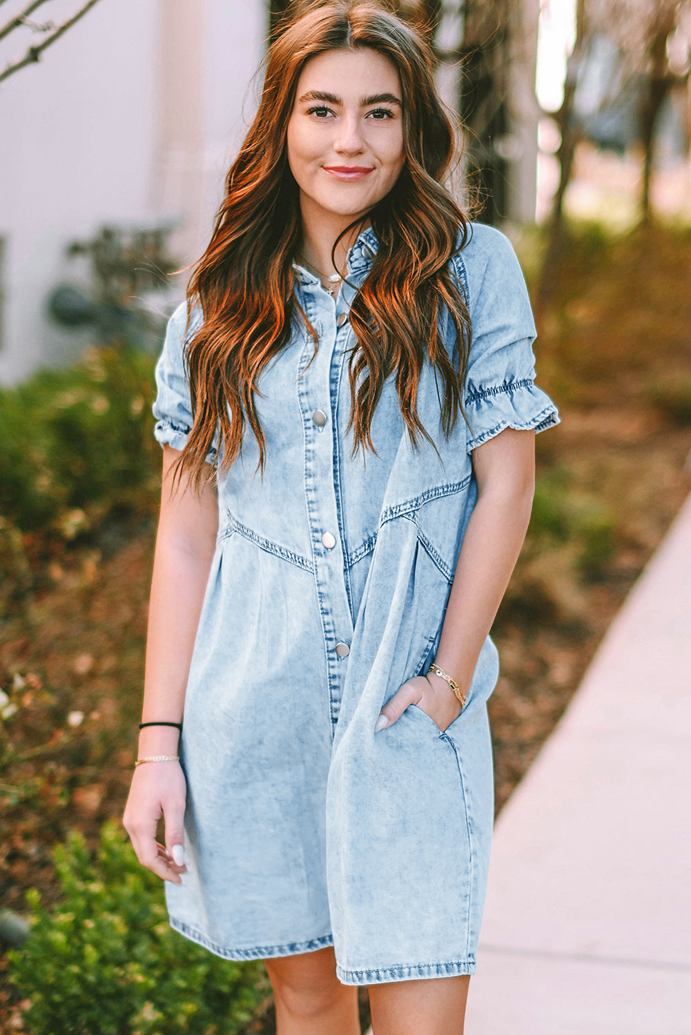 Model walking on the beach in a blue mineral washed denim dress with ruffled short sleeves and pockets.