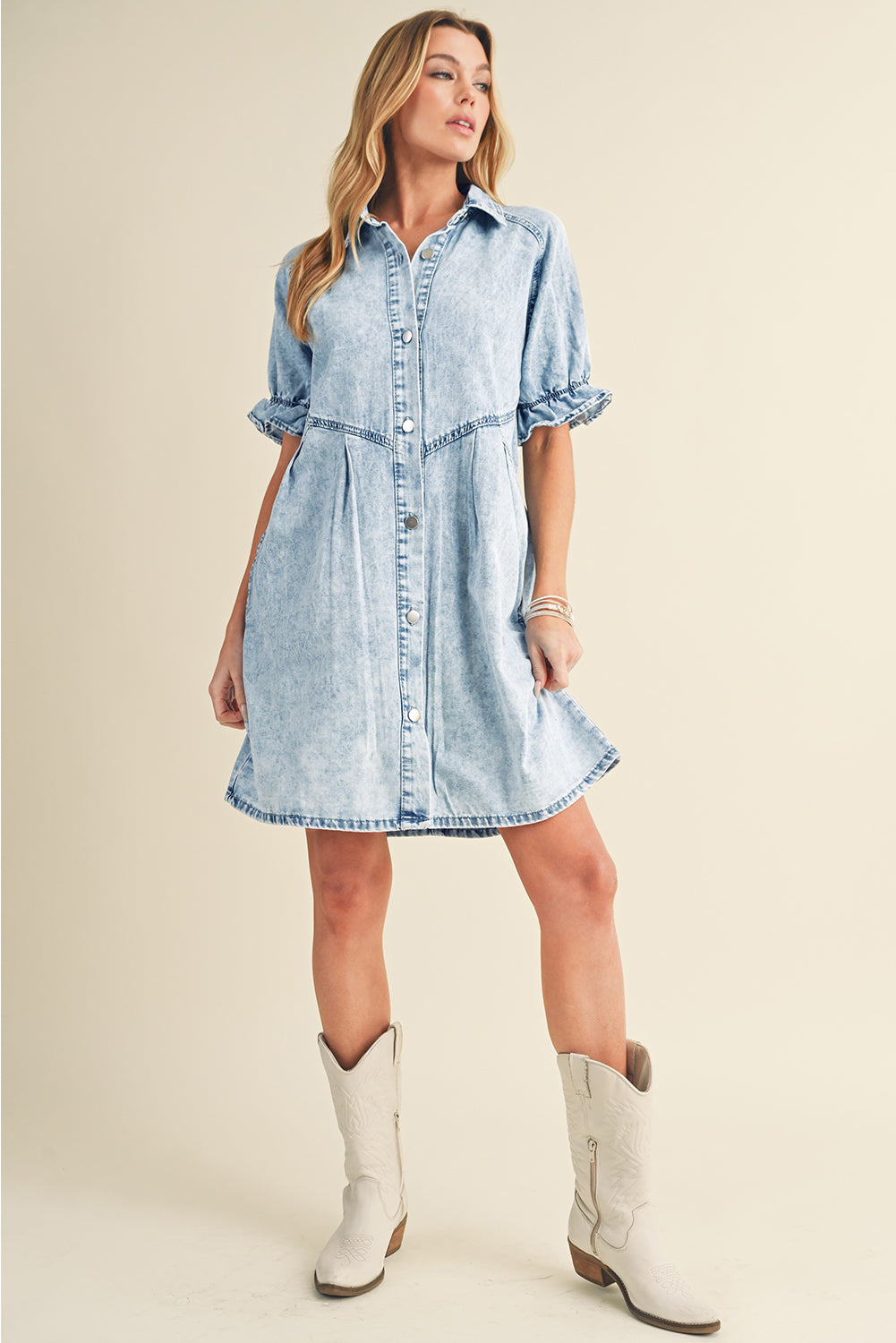 Blue mineral washed denim dress with ruffled short sleeves and pockets hanging neatly on a hanger.