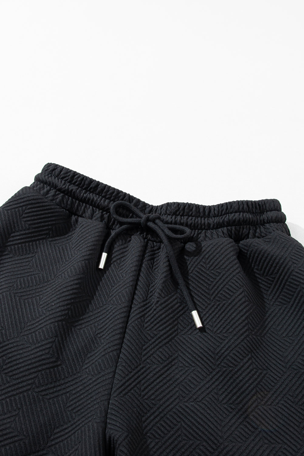 Close-up of the hemline on the black textured wide-leg pants.