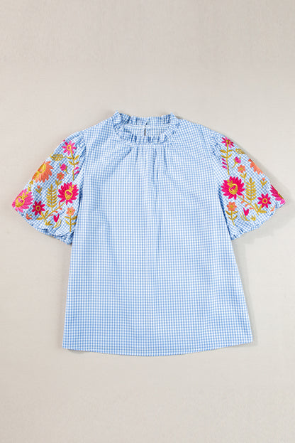 Close-up of the intricate floral embroidery design on the light blue gingham blouse.