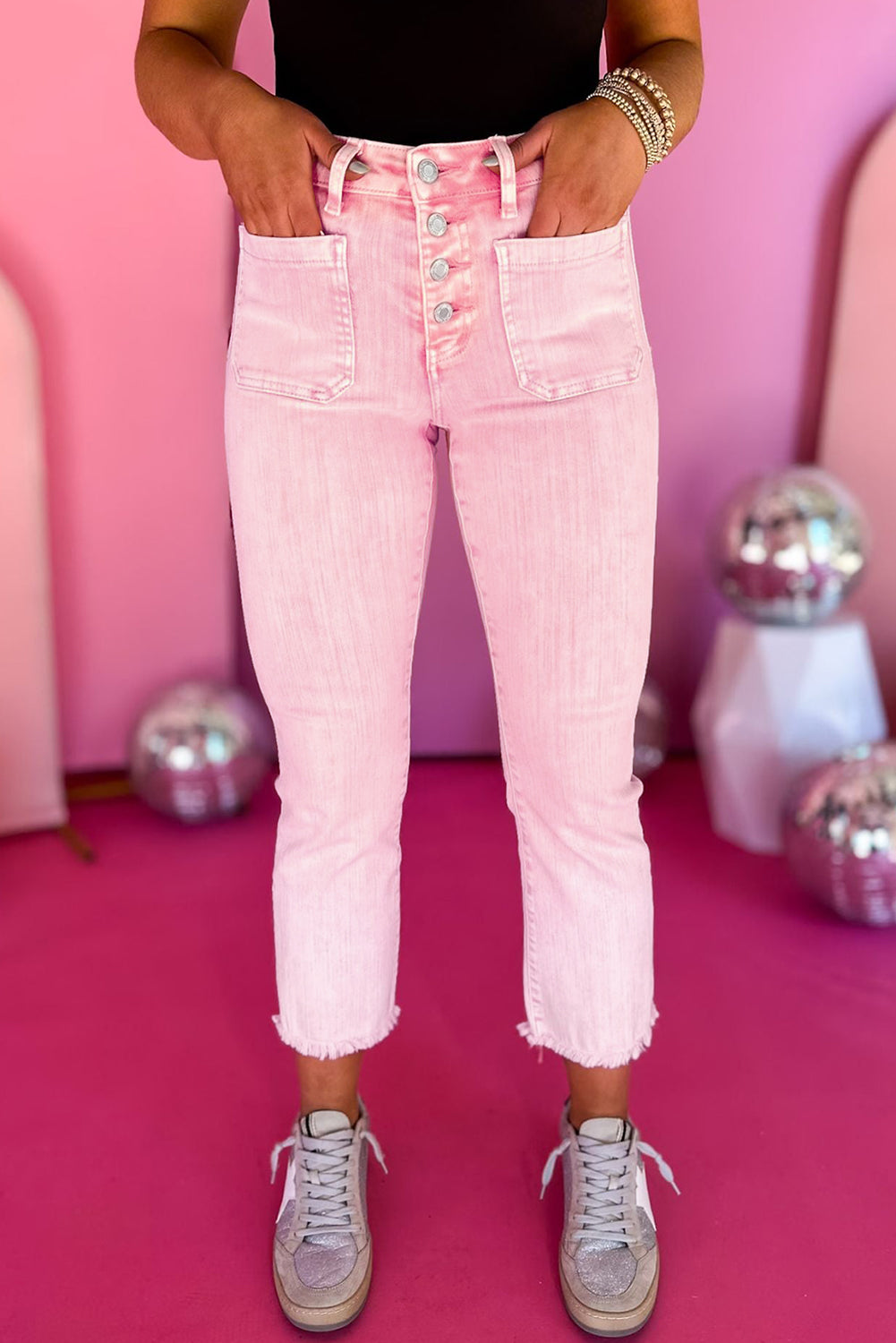 Model wearing high-waisted apricot pink crop jeans with multiple buttons and a raw edge, paired with white sneakers