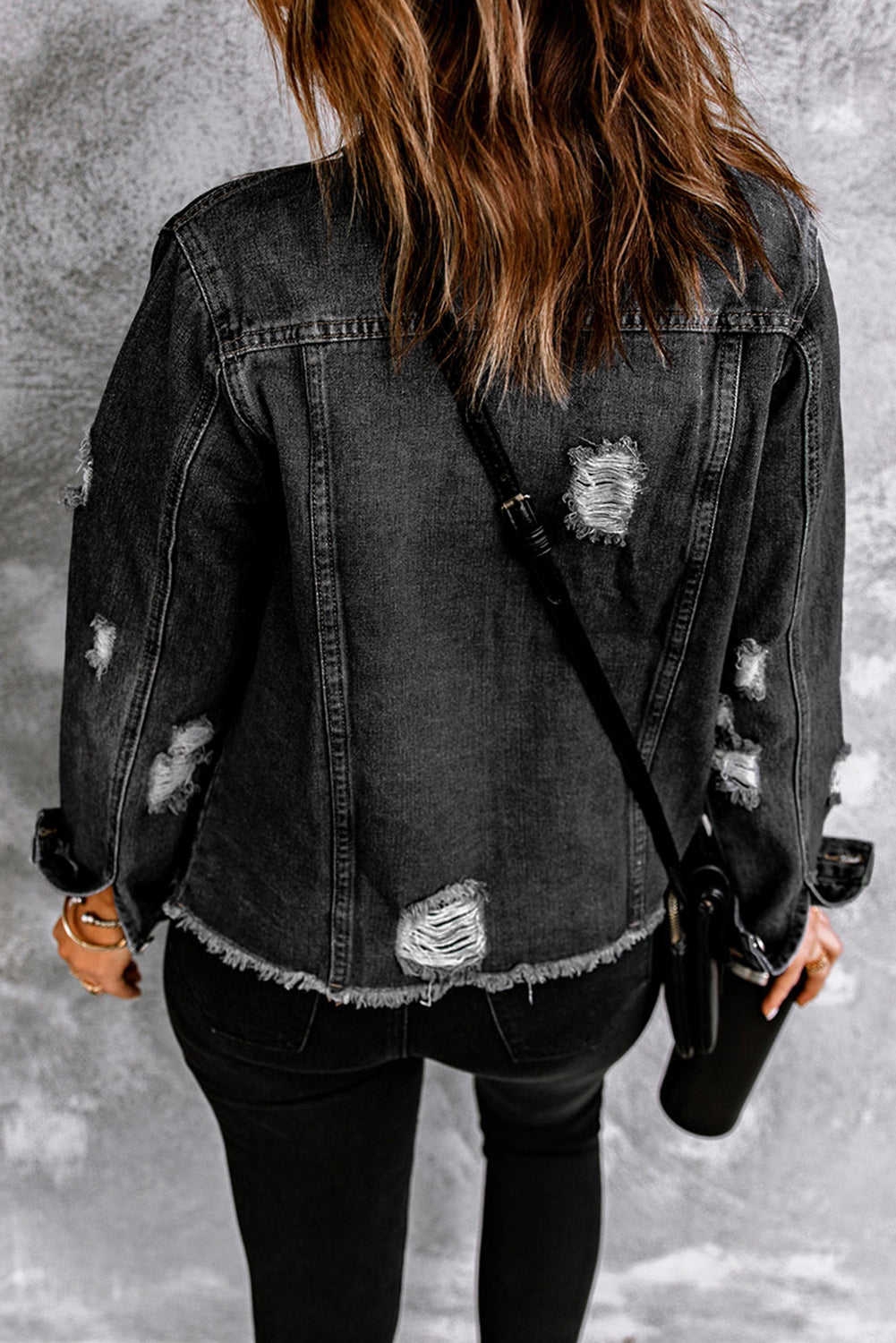 Close-up of black denim jacket with distressed details.